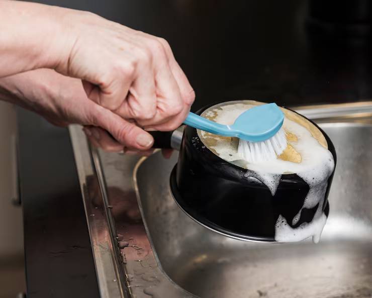 Scrubbing soapy cookware with a dish brush.