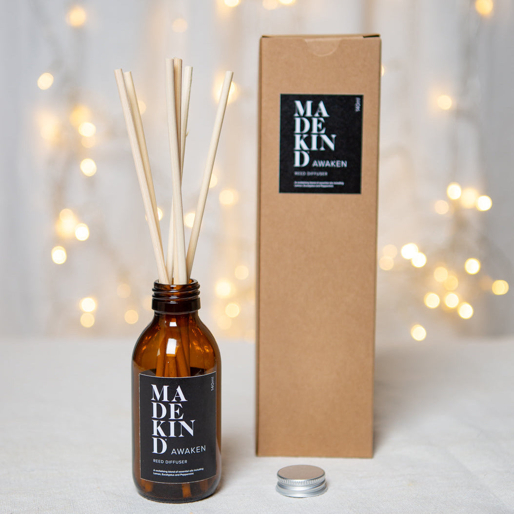 Photo of awaken reed diffuser bottle with lid of and box and twinkly christmas lights