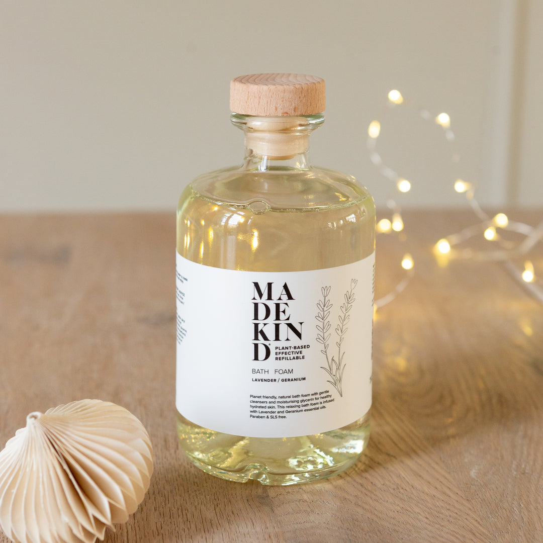 Bottle of 'MADEKIND' bath foam on a wooden surface with decorative lights in the background