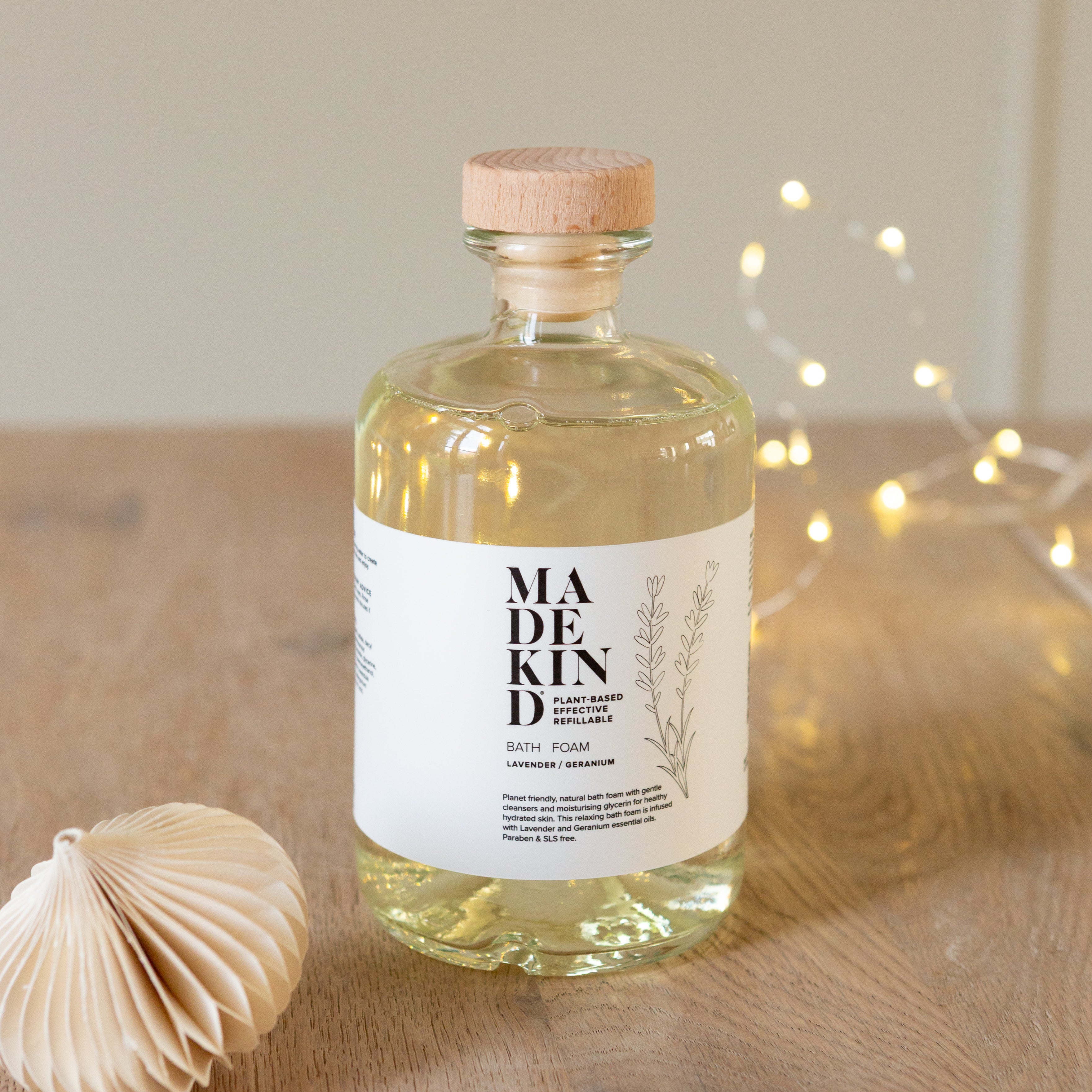 Bottle of 'MADEKIND' bath foam on a wooden surface with decorative lights in the background