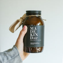 Load image into Gallery viewer, Photo of a hand holding MadeKind bath salts in an amber glass bottle
