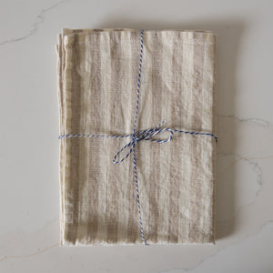 Photo of a woven line beige and white striped tea towel, folded and tied with twine