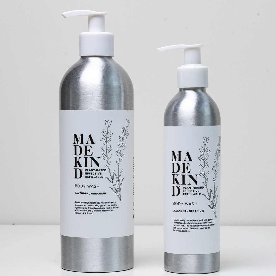 Two silver pump bottles of MADE KIND body wash with white labels, one larger and one smaller, standing on a white surface against a light gray background.