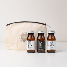 Load image into Gallery viewer, Photo of cotton pouch with MadeKind logo and 3 mini toiletries. 60ml amber glass bottles of shampoo, body wash and hand wash.
