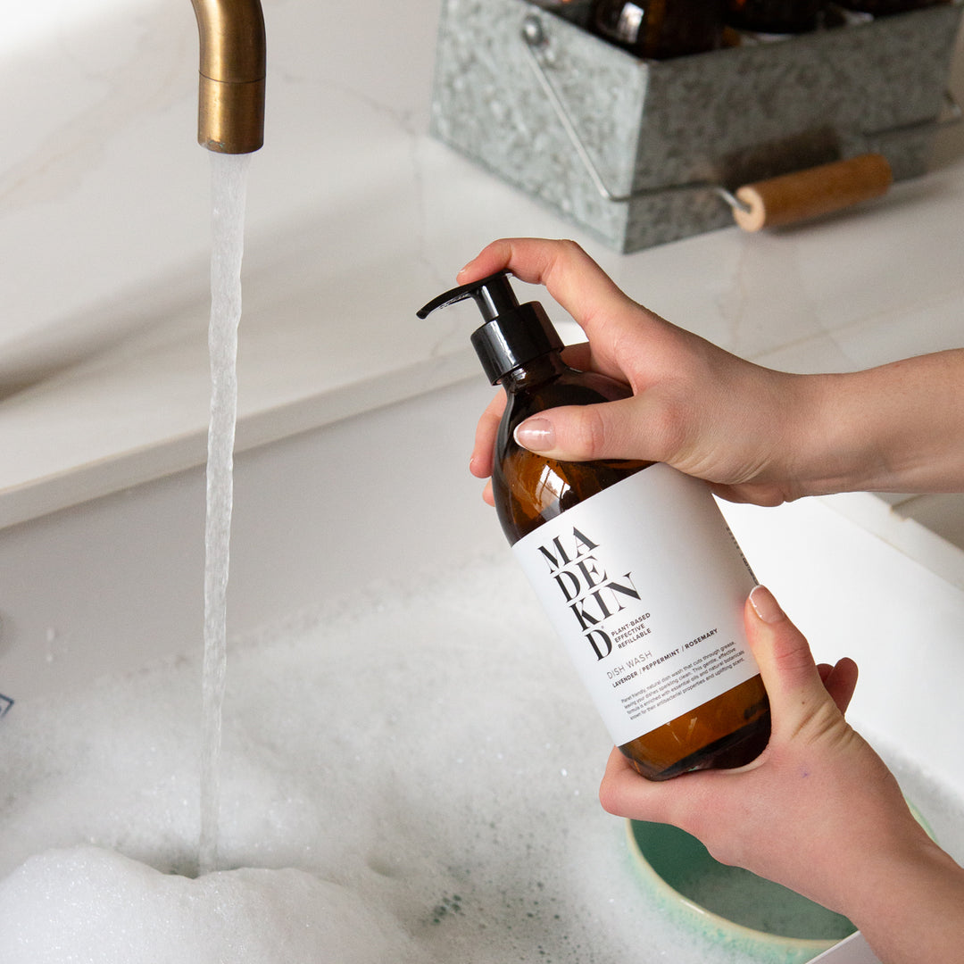 Person holding a MadeKind Dish Wash bottle under running water.