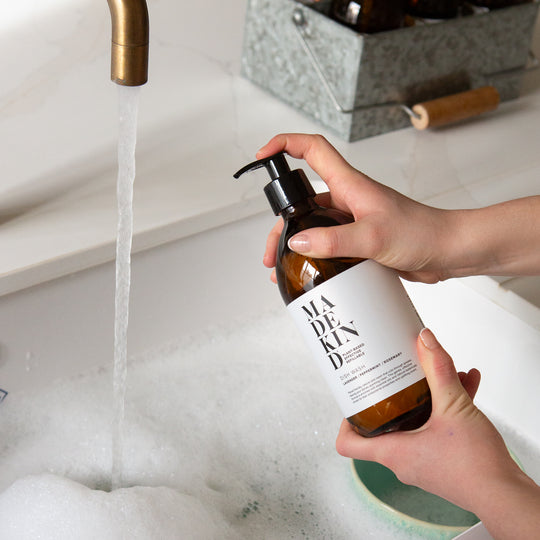 Person holding a MadeKind Dish Wash bottle under running water.