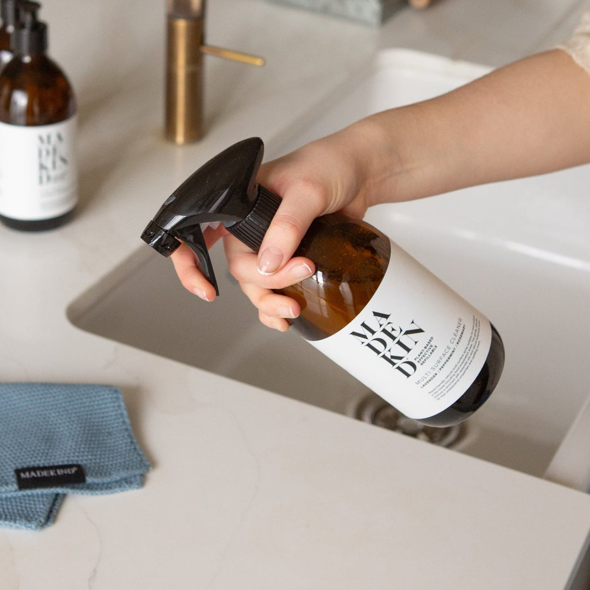 Photo of a hand holding a bottle of Multi Surface Cleaner at a kitchen sink