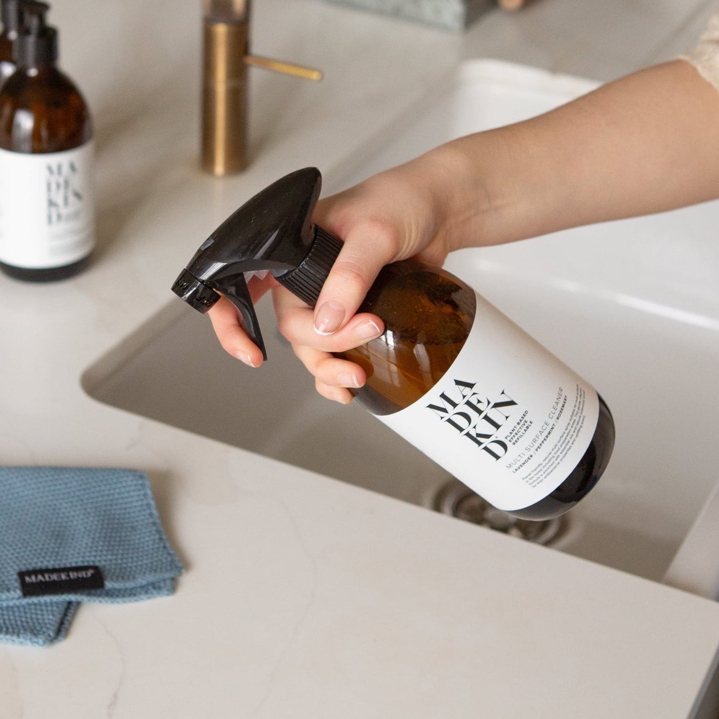 Photo of a hand holding a bottle of Multi Surface Cleaner at a kitchen sink