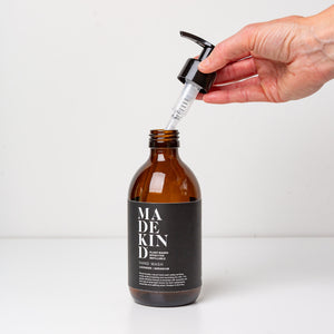 Photo of empty 300ml amber glass bottle with a hand holding the pump for lavender and geranium hand wash or hand lotion