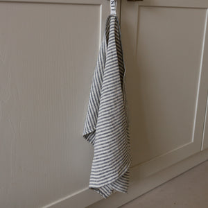 Photo of a woven linen grey striped tea towel hanging from a hook in a kitchen