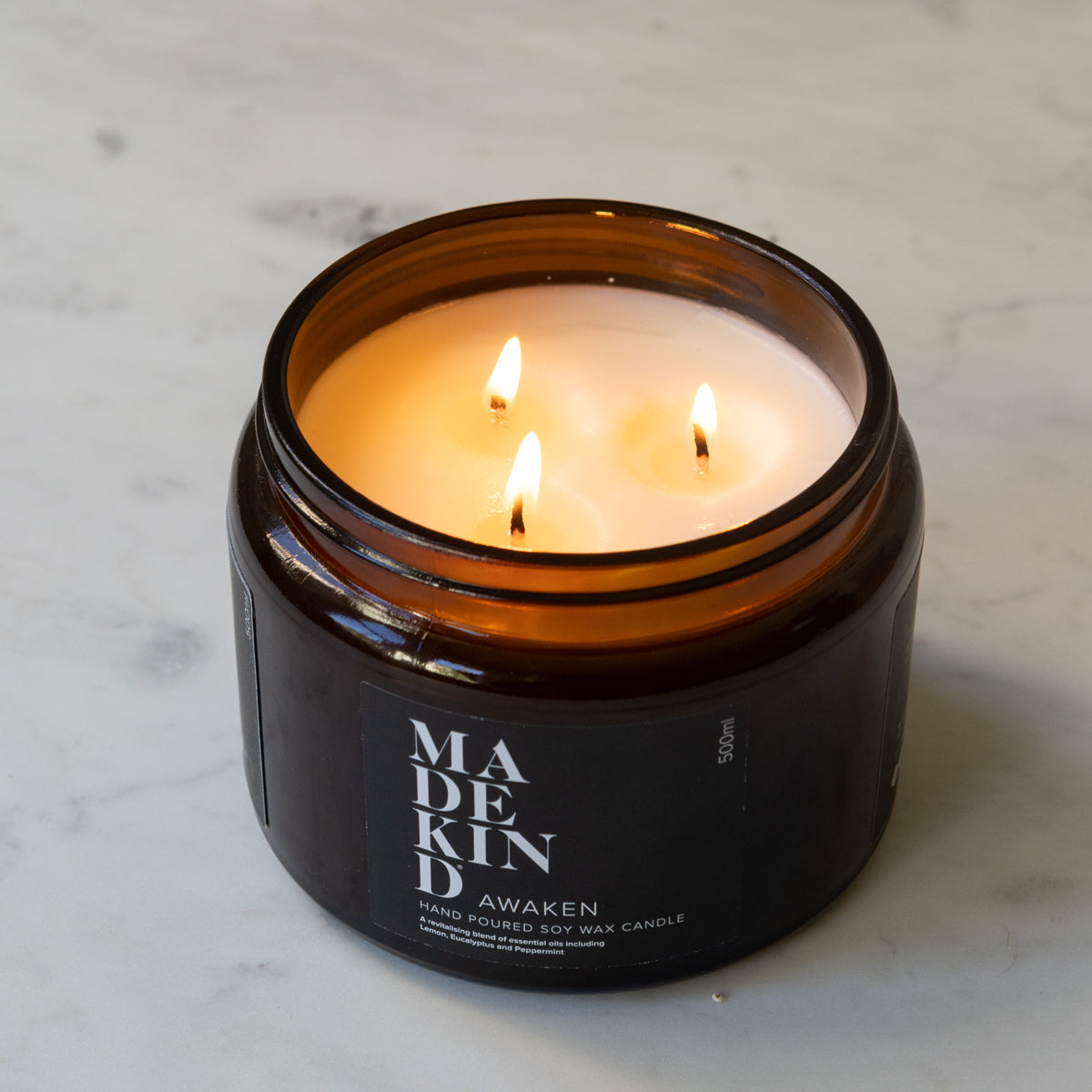 A lit three wick soy wax MadeKind candle in an amber glass jar .