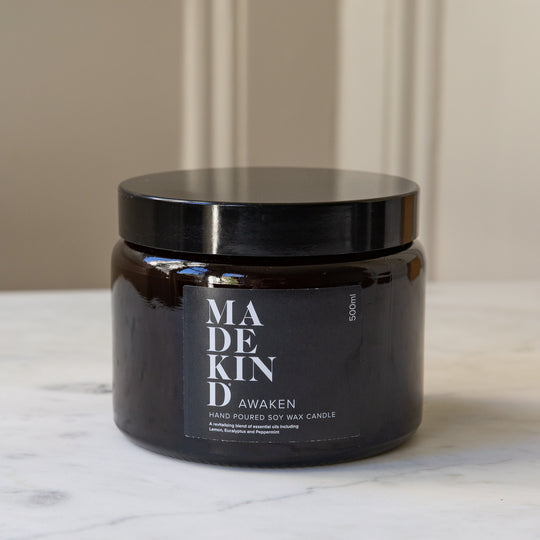An amber glass jar MadeKind soy wax candle with a black lid and with three wicks on a light marble surface. 