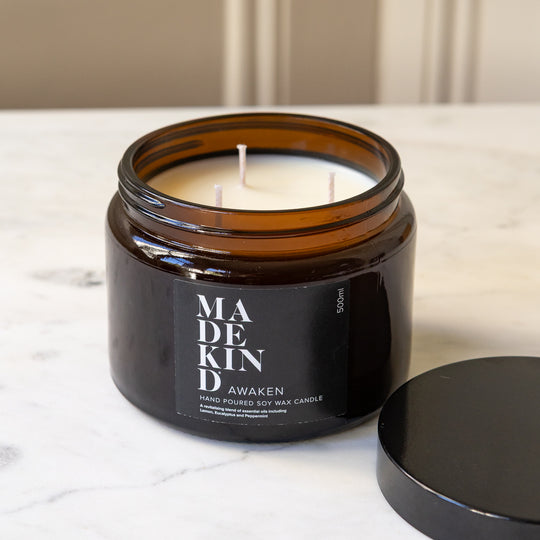 An unlit amber glass jar candle with three wicks sits on a white marble table  with black lid sitting next to it.