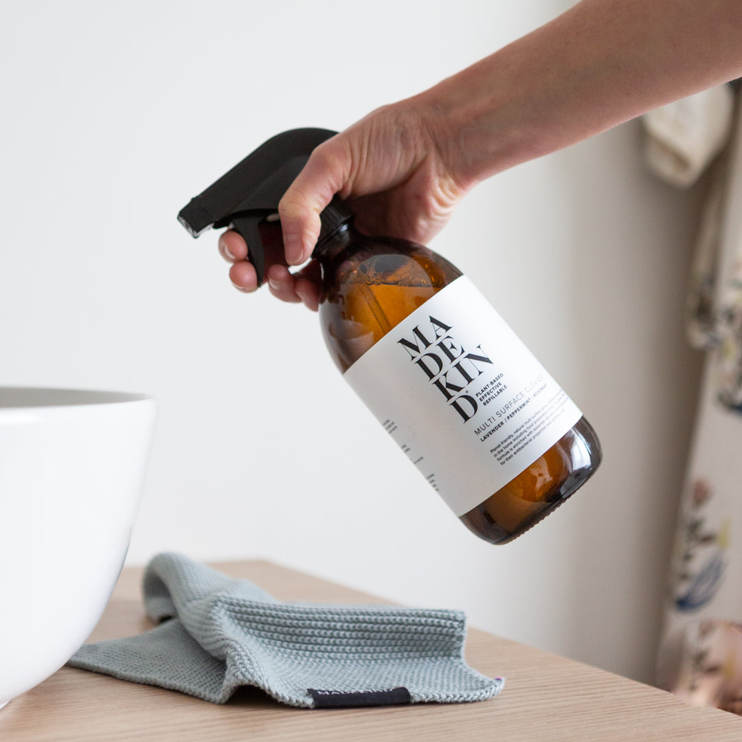 Photo of a hand holding a MadeKind Bathroom Cleaner in an amber glass spay bottle, spraying into a bathroom sink