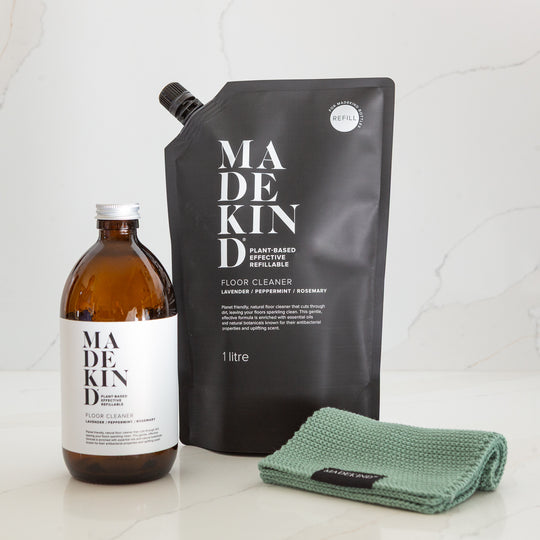 MadeKind floor cleaner glass bottle, refill pouch, and green cloth on a light background. eco friendly cleaning products.