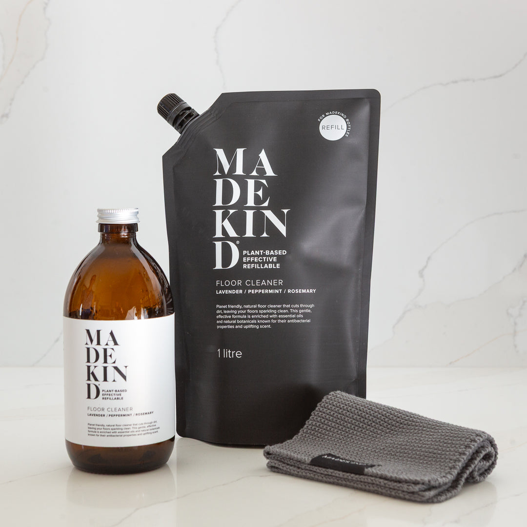 MadeKind floor cleaner glass bottle, refill pouch, and grey cloth on a light background. eco friendly cleaning products.