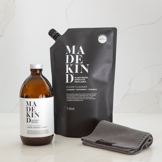 MadeKind floor cleaner glass bottle, refill pouch, and grey cloth on a light background. eco friendly cleaning products.