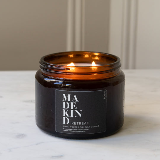 A lit amber glass jar MadeKind candle on a white marble surface with a neutral beige panelled wall in the background.