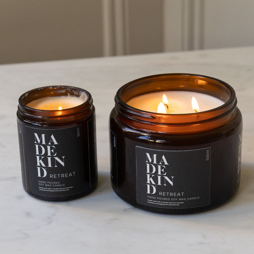 Two amber glass jar MadeKind candles on a light marble surface, one small 180ml Retraet candle and one large 500ml Retreat candle.