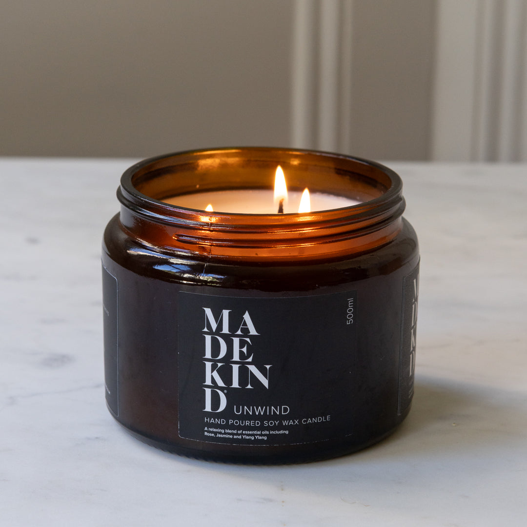 A lit amber glass jar MadeKind soy wax candle with three wicks on a light marble surface. 