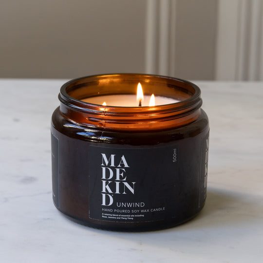 A lit amber glass jar MadeKind soy wax candle with three wicks on a light marble surface. 