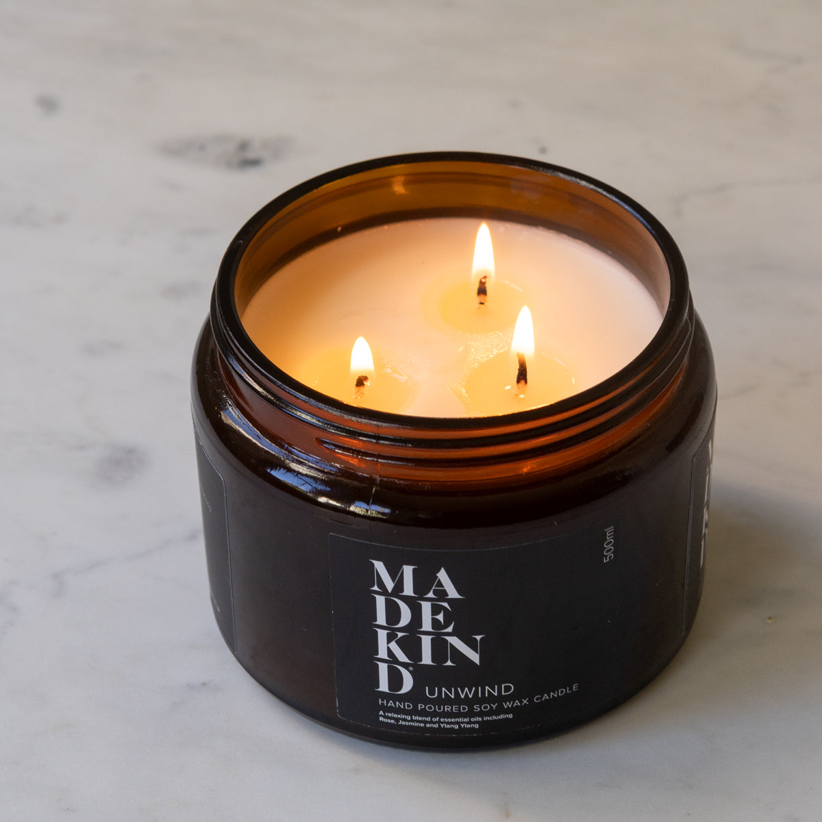 A lit amber glass jar MadeKind soy wax candle with three wicks on a light marble surface. 
