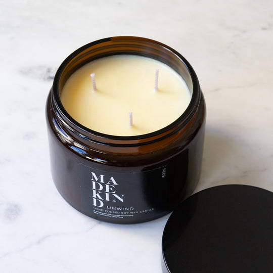 An amber glass jar MadeKind soy wax candle with three wicks on a light marble surface. The lid is off showing three unlit wicks.