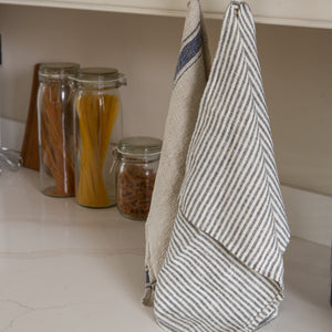 Photo of a woven linen grey striped tea towel and a rustic tea towel hung in a kitchen