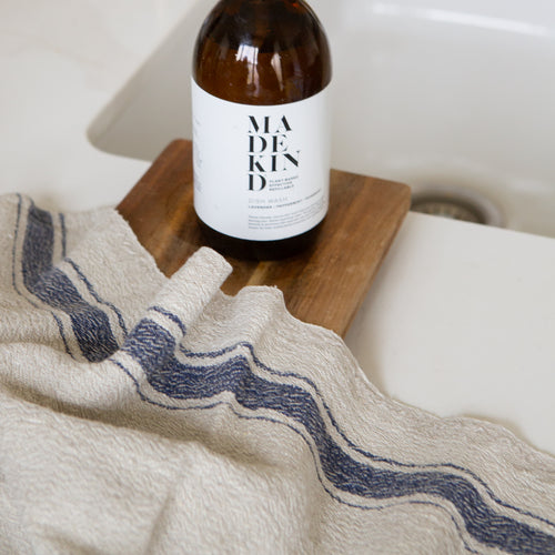 Photo of a woven line tea towel with a navy blue stripe next to a kitchen sink