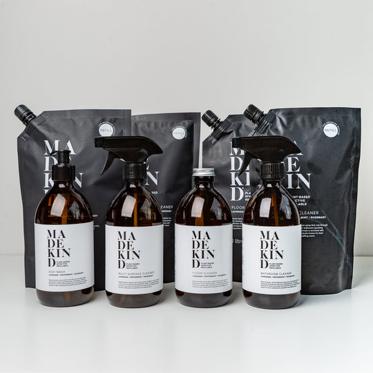 Four amber 'forever' bottles with MadeKind labels, next to four refill pouches of natural cleaning refills, all branded MadeKind.