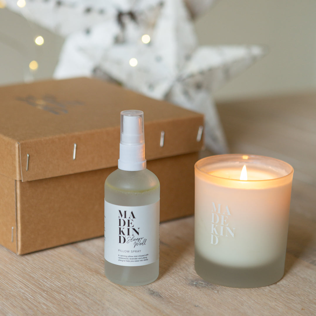 Madekind pillow mist and soy wax aromatherapy sleep well candle on a wooden surface next to a gift box with a blurred starry background