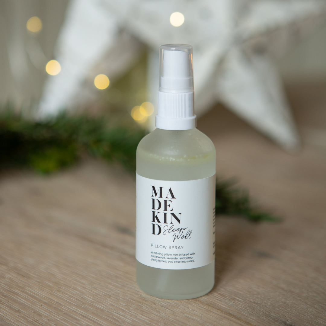 Bottle of Made Kind pillow spray on a wooden surface with blurred lights in the background