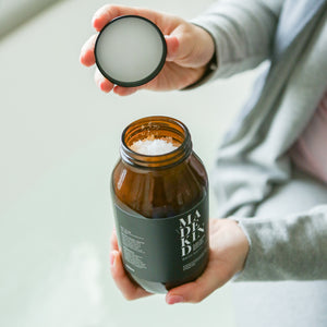 Photo of a person holding an amber glass bath salts jar full of salts with the other hand holding the lid