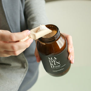 photo of a hand scooping MadeKind bath salts from an amber glass jar containing bath salts
