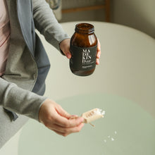 Load image into Gallery viewer, Photo of a person holding an amber glass jar full of bath salts whilst they are holding a scoop full of bath salts over a bath
