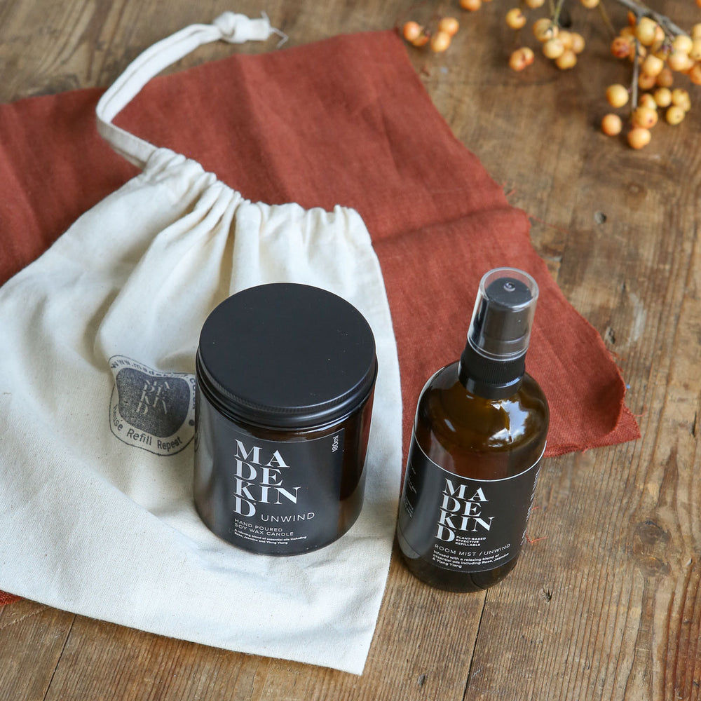 Photo of unwind amber glass bottle next to a room mist spray bottle on top of a gift bag on a wooden table