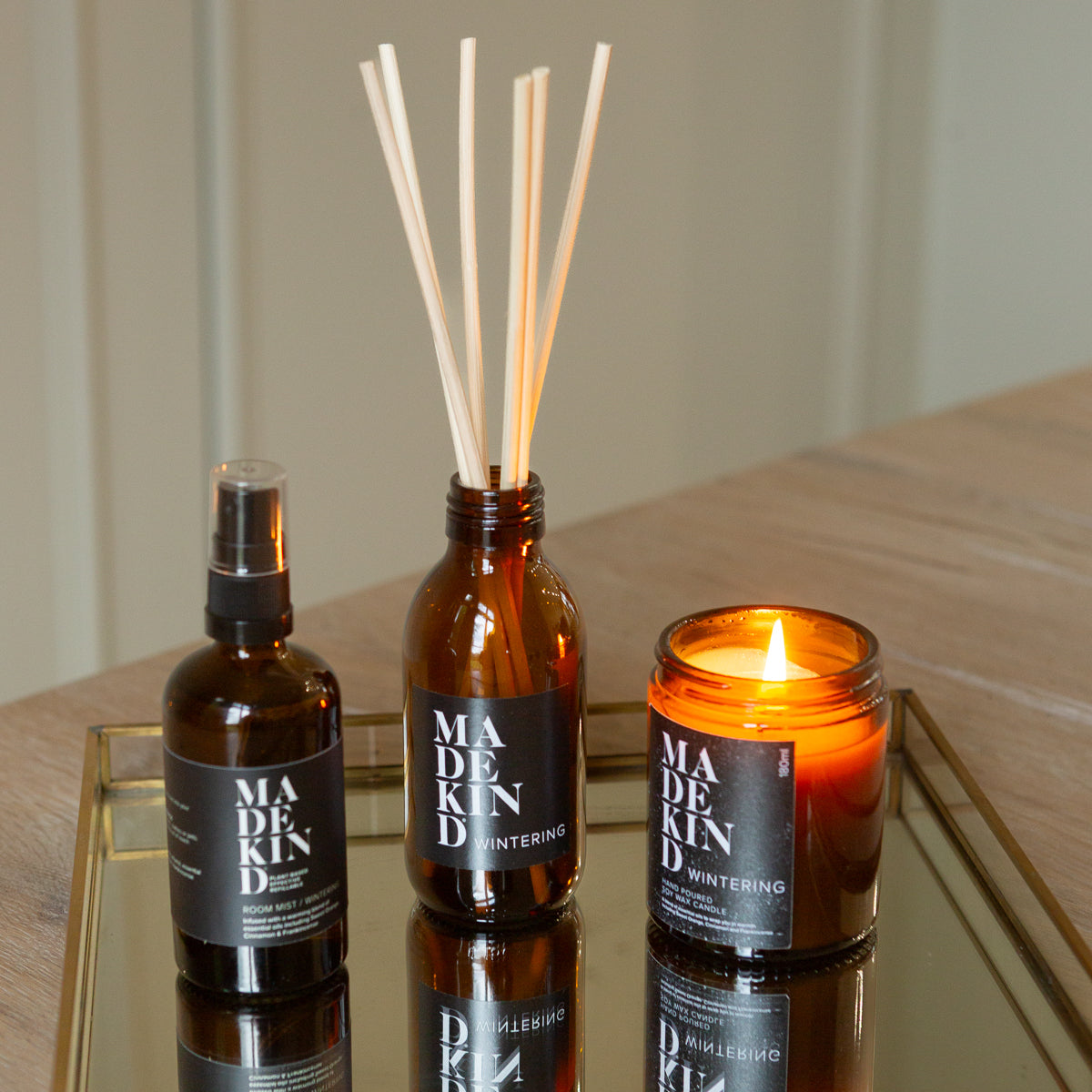 Three 'MADEKIND' products including a bottle, diffuser, and candle on a reflective surface.