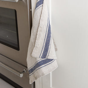 Photo of he madekind blue border striped tea towel next to an oven