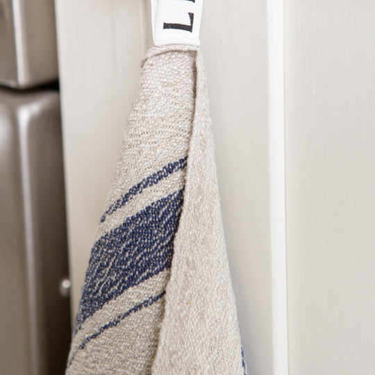 Photo of a blue striped woven linen tea towel hanging from a hook in a kitchen