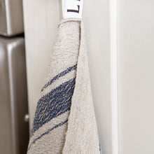 Load image into Gallery viewer, Photo of a blue striped woven linen tea towel hanging from a hook in a kitchen
