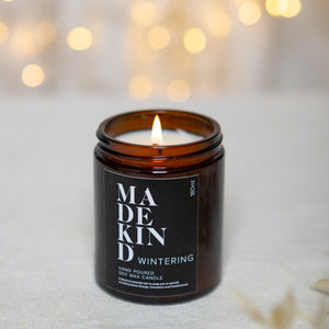 photo of 180ml MadeKind wintering candle, lit and with sparkly lights in the background